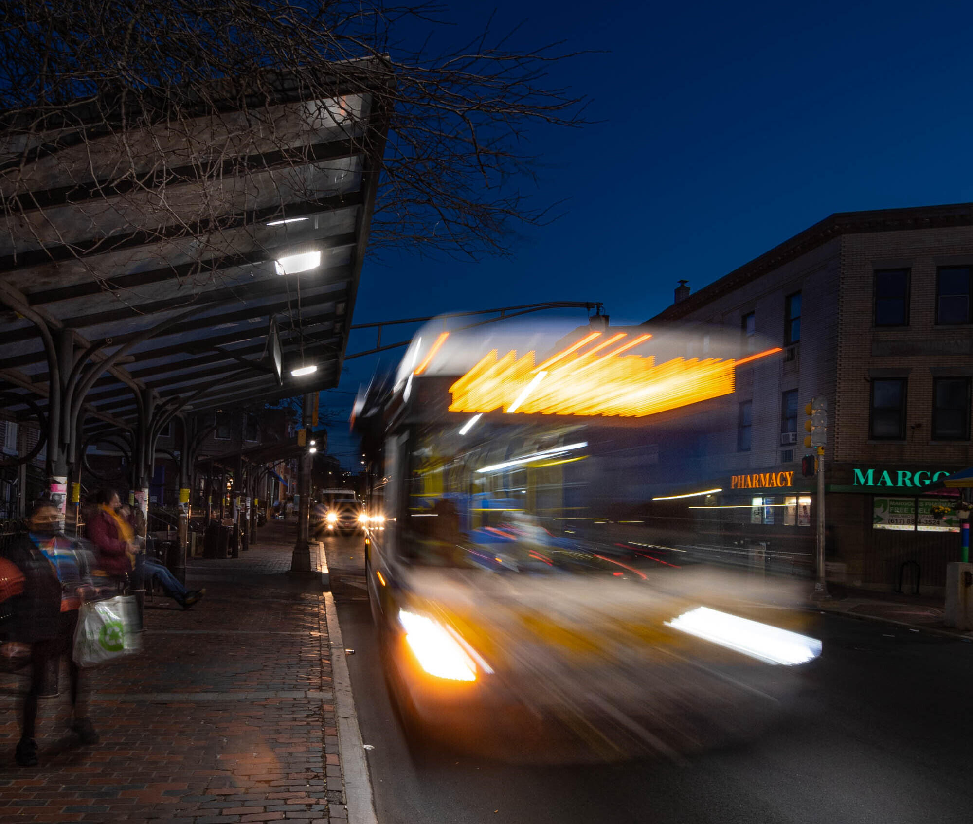 A bus at night in Chelsea drives away from a bus stop