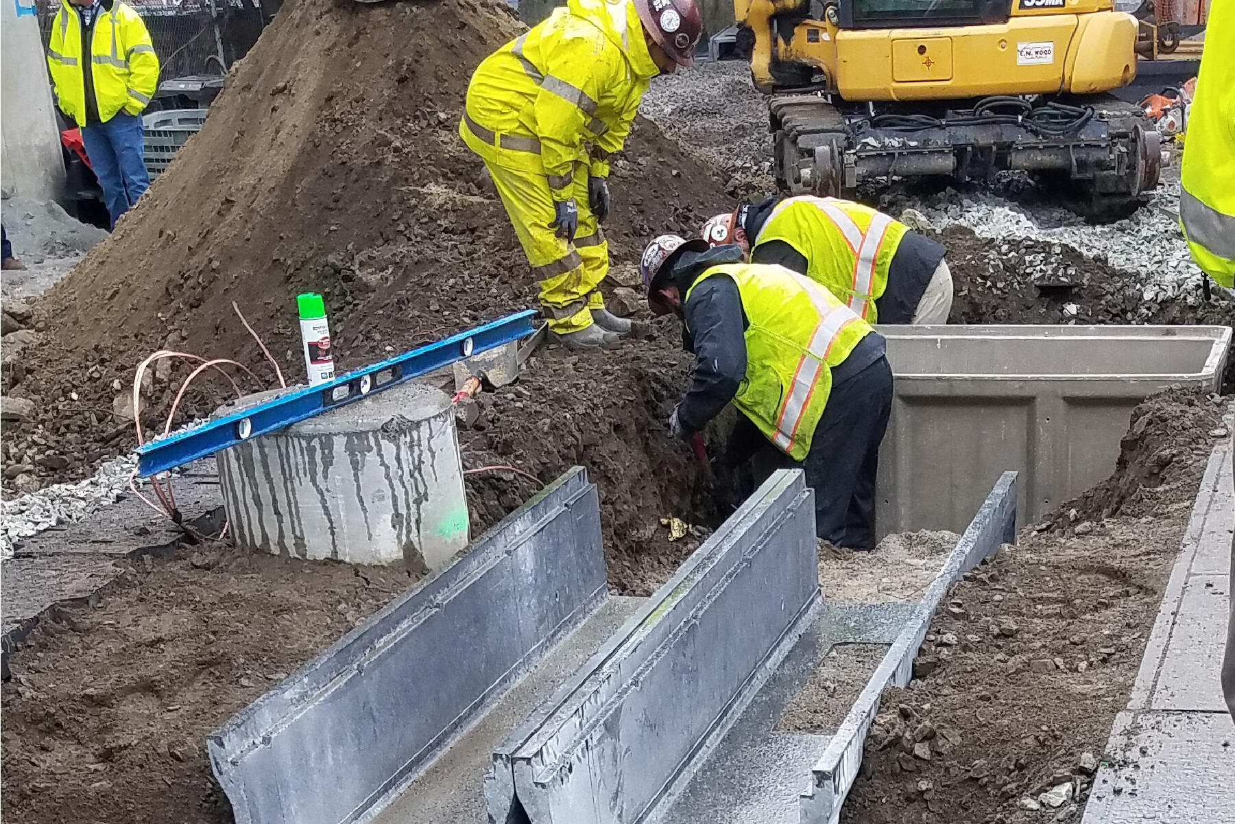 three crew members working together on ductbank in a dirt ditch on a rainy day