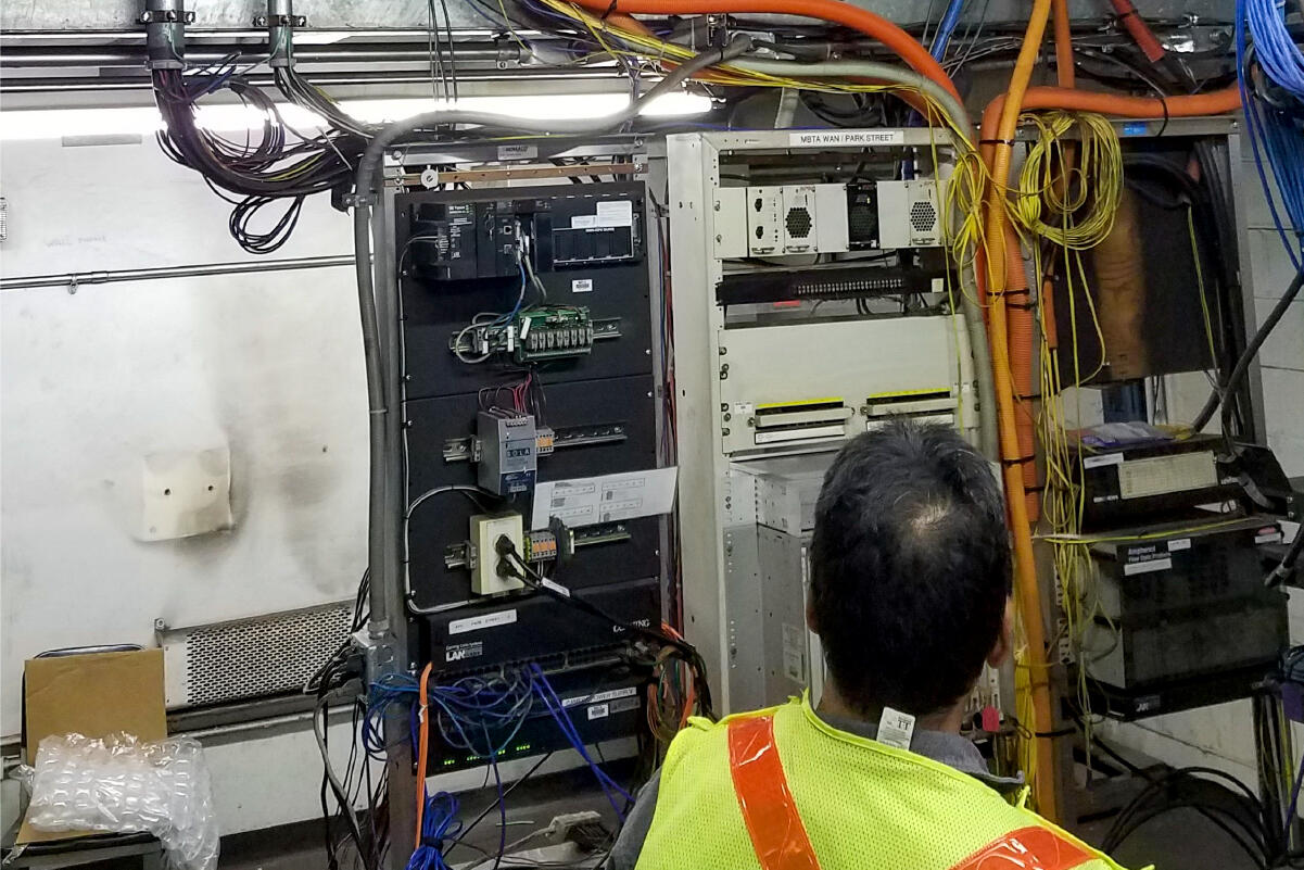 a person in a reflective vest looking at a wall of signal equipment (switches, wires, outlets)