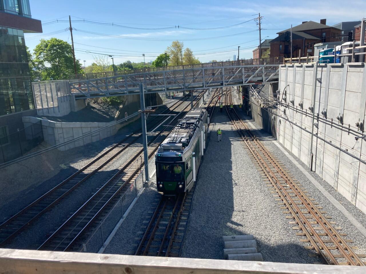 A green line test train passes under the pedestrian bridge at Tufts University