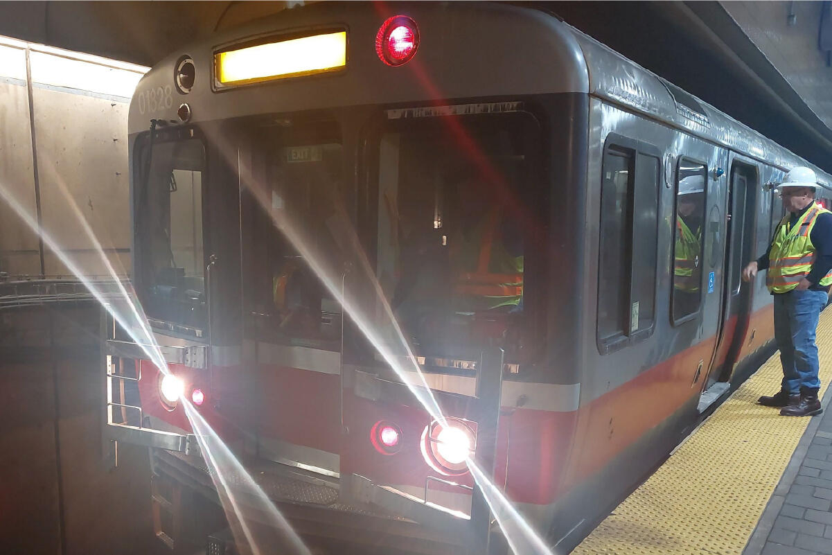 a crew member in a reflective vest stands outside a red line train talking to an operator inside 