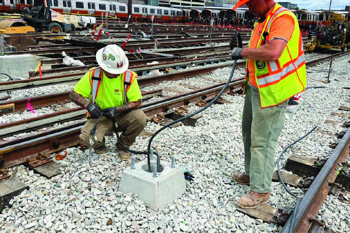 two crew members working on wiring between train tracks outside