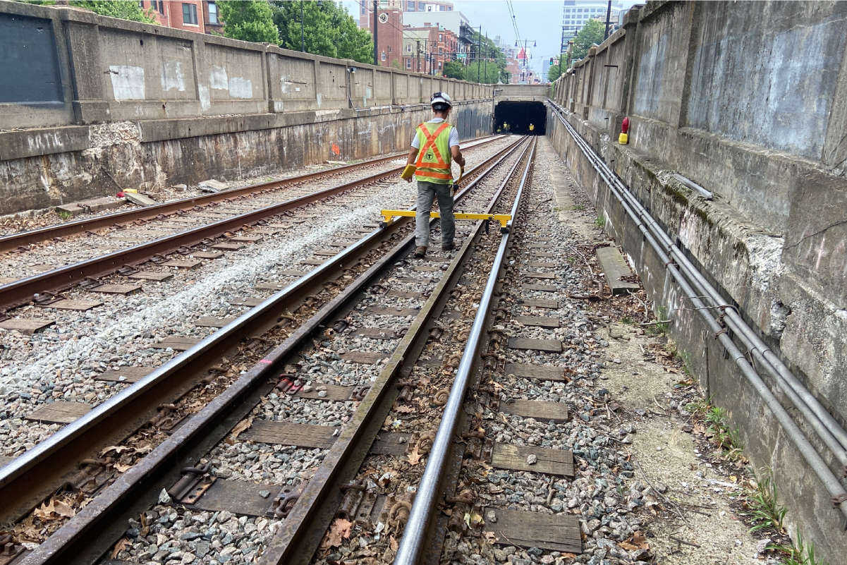 a construction worker wearing a hard hat and reflective vest stands on tracks near a tunnel