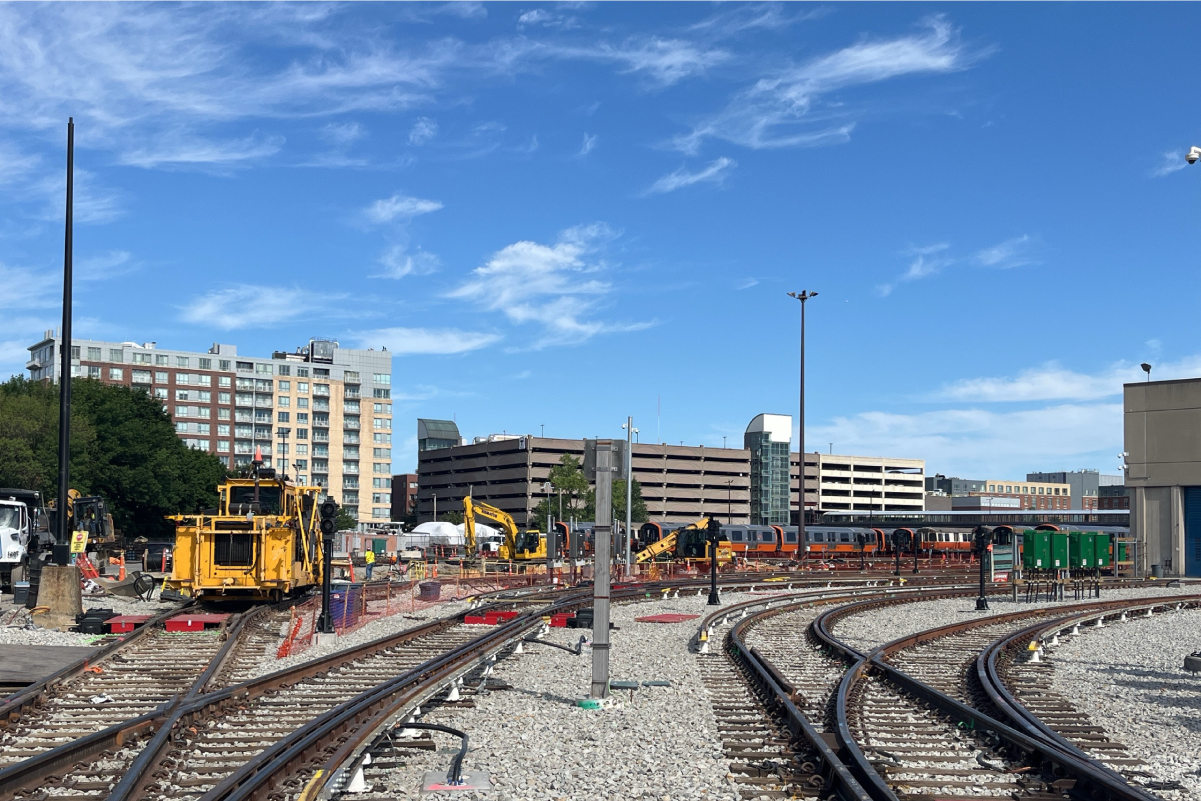 many sets of tracks outside on a sunny day, with orange line trains parked on them in the distance