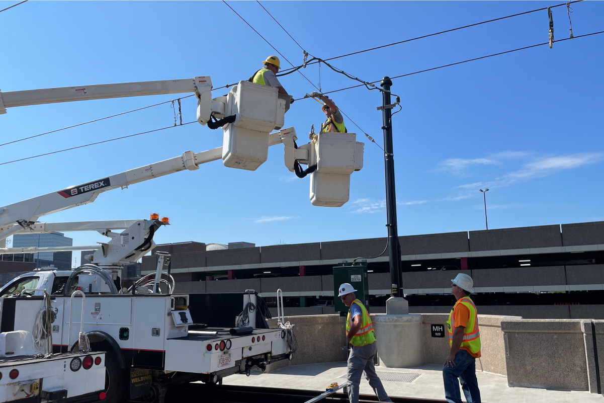 crews in lifts working on overhead signal wires with a blue sky above