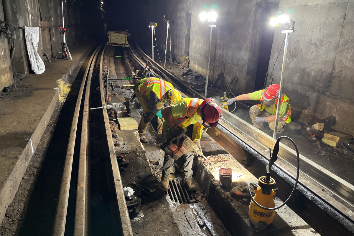 crews working on tracks under floodlights in a tunnel