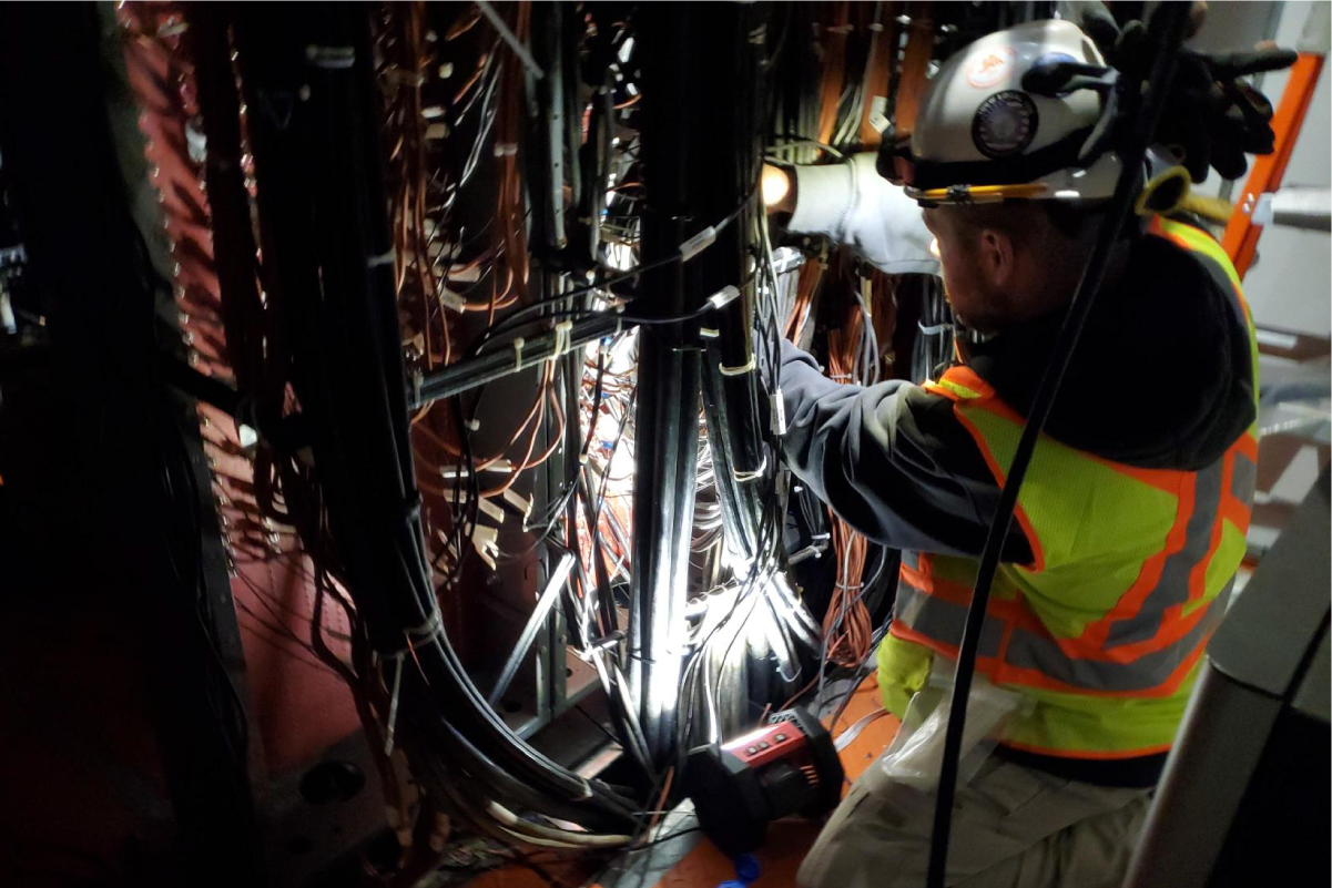 a crew member working on wires in the dark using a headlamp on their hard hat
