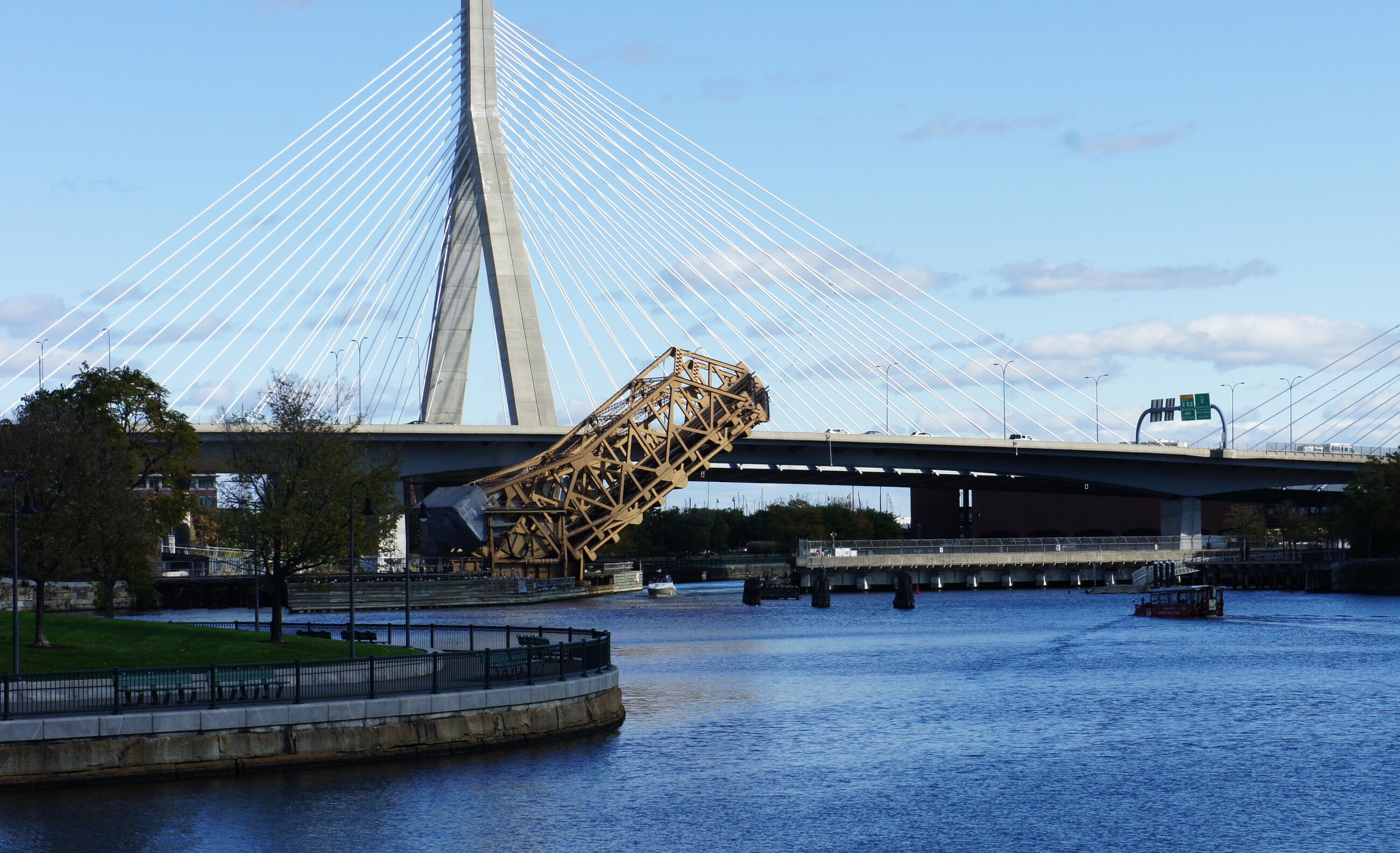 a bridge near north station is partially raised over water. the zakim bridge is in the background