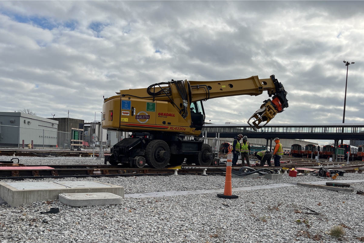 four crew workers in reflective vests and hard hats working on tracks next to a large piece of machinery