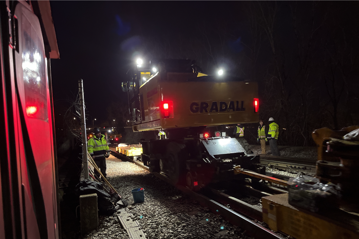 crews surround heavy equipment on rail at night under floodlights