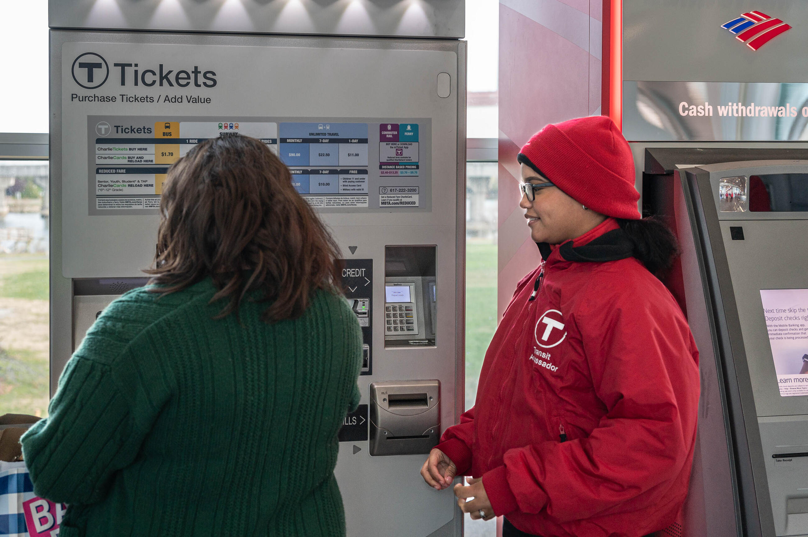 Transit ambassador in a red jacket helping rider at a fare vending machine at Assembly station