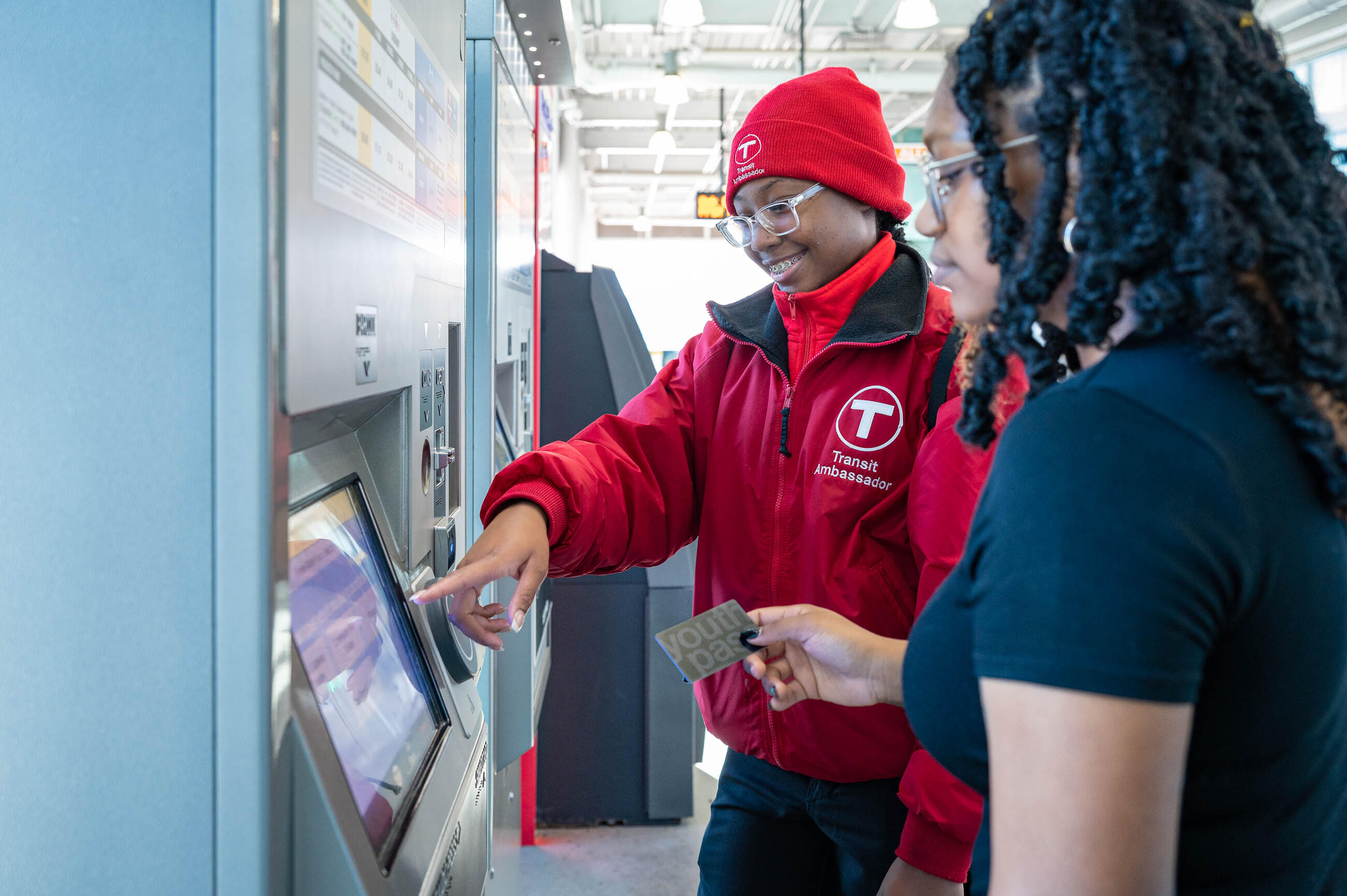 Transit Ambassador in red jacket pointing at fare vending machine with rider