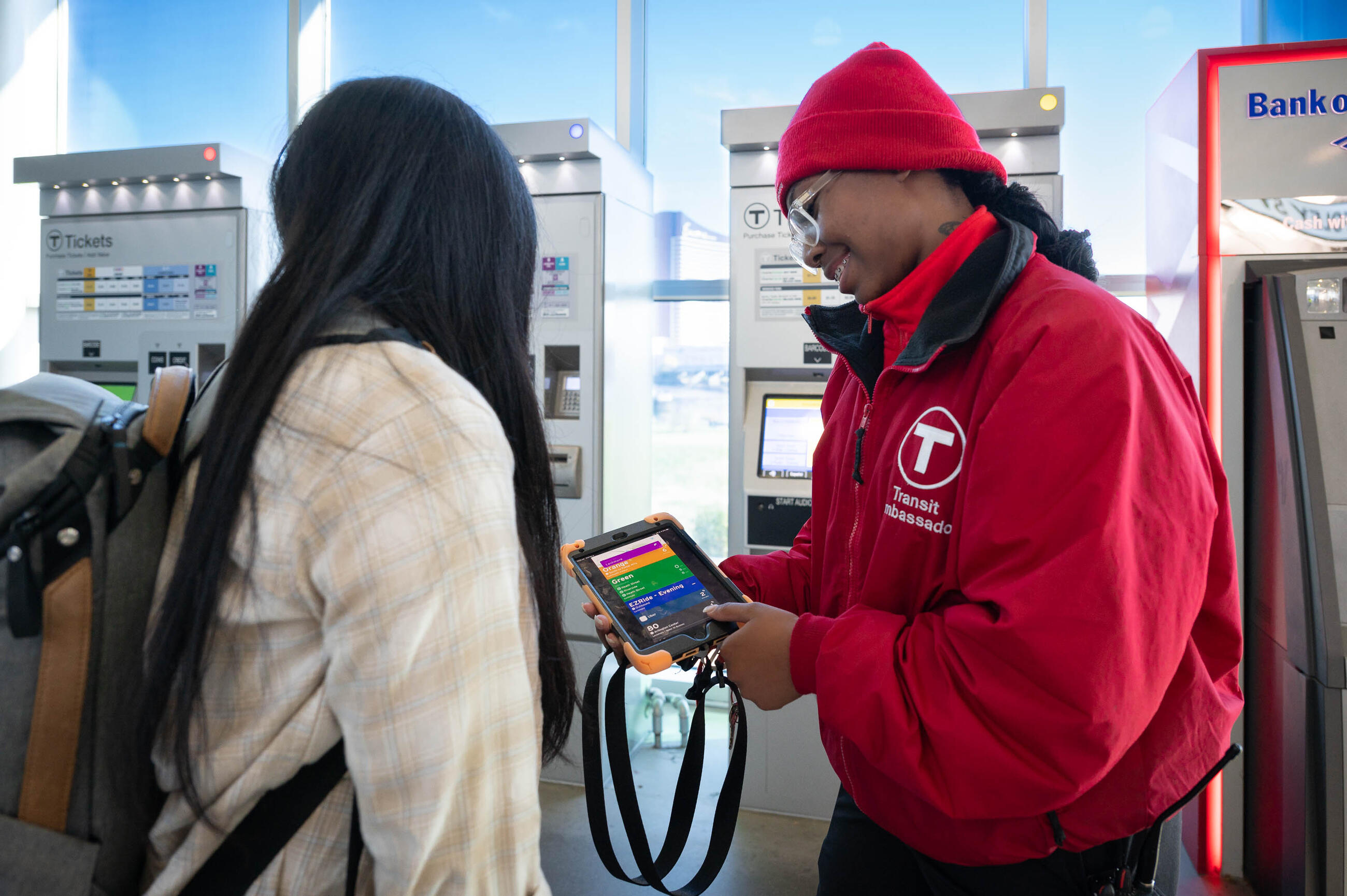 Transit Ambassador in red jacket using a tablet to help a rider