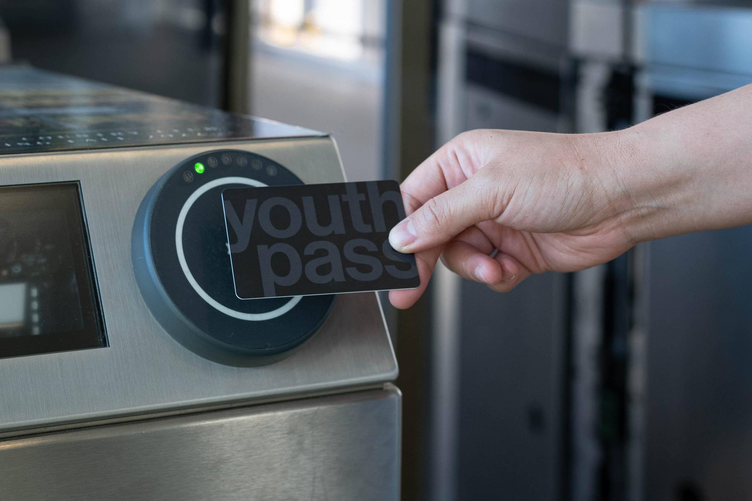  Hand holding black and grey Youth Pass and tapping at fare gate 