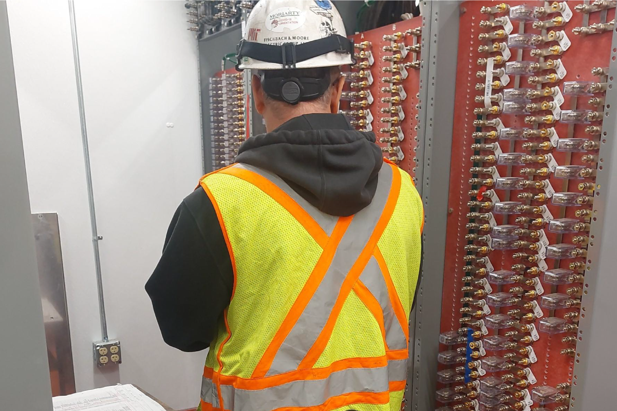 crew member in reflective vest and hard hat facing a wall of electronic switches
