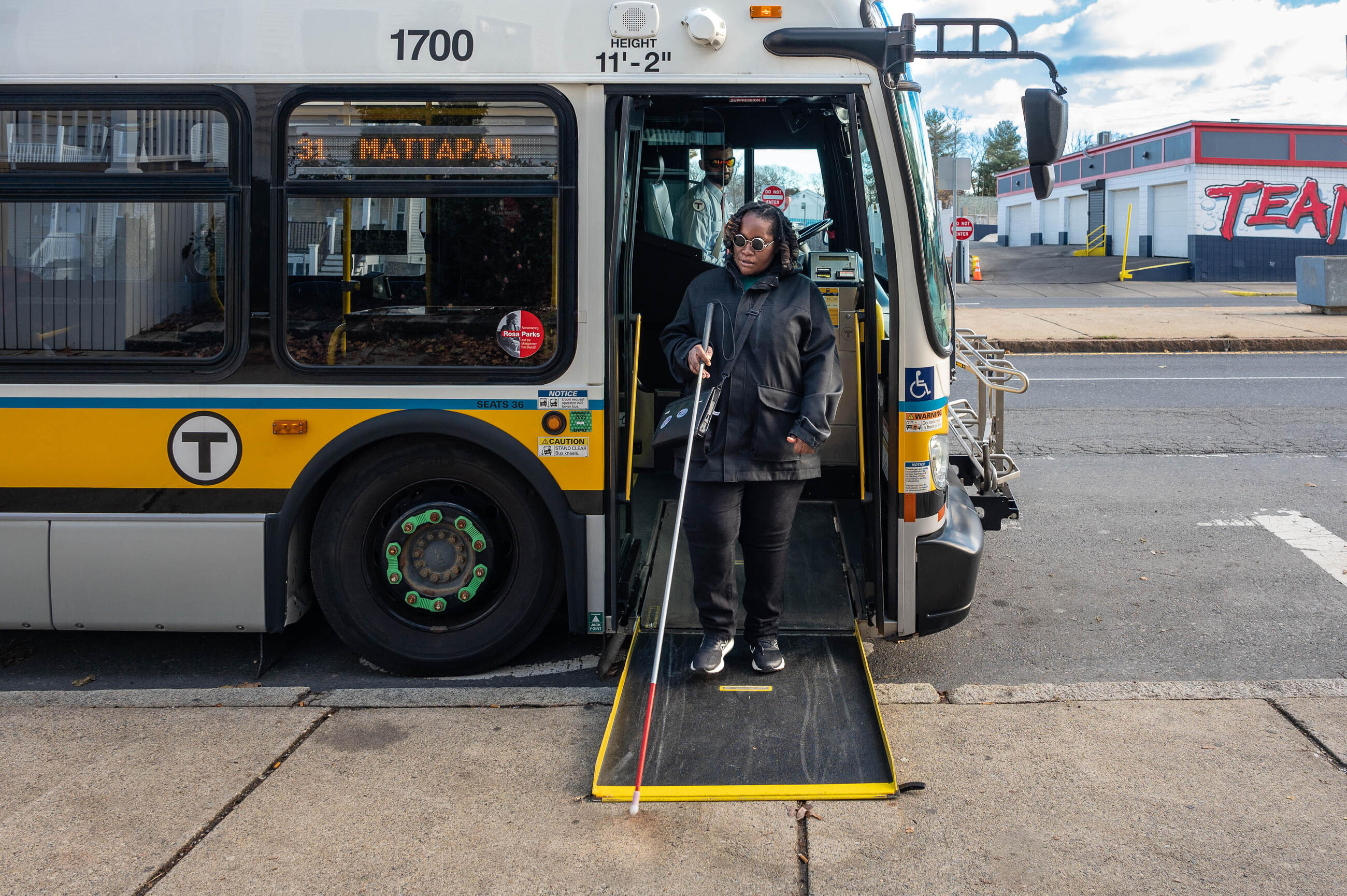 a blind or low vision rider using a white cane while exiting a Mattapan-bound bus via the bus door ramp
