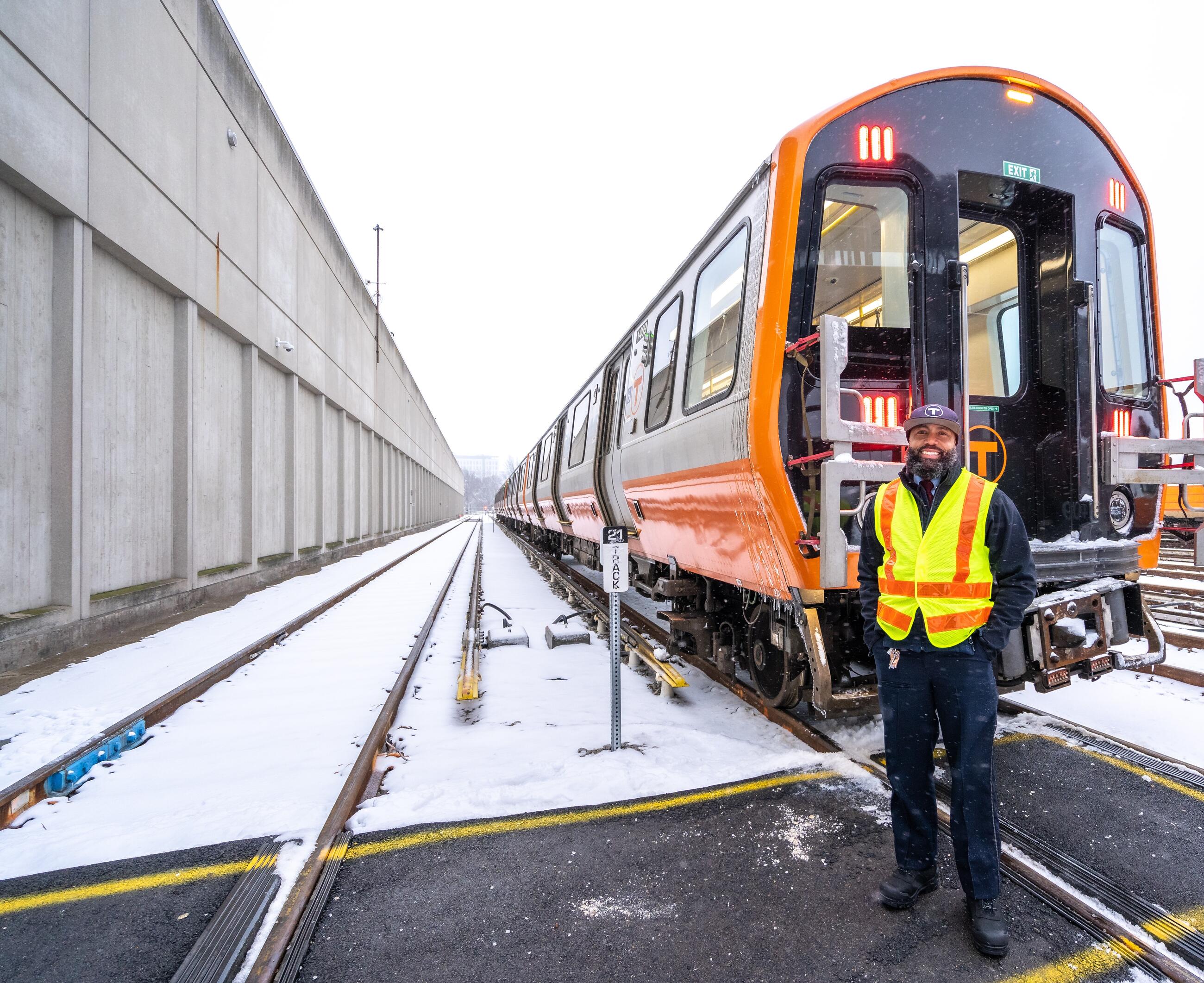 Transit driver standing in front of car stopped on the tracks. Snow on the ground behind it.