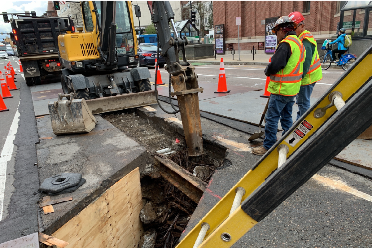 two crew members looking down a rectangular hole cut into the street