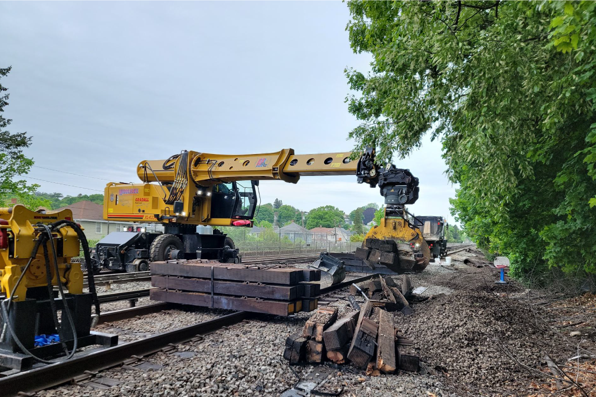 crew using large construction machinery to pick up a pile of wooden railroad ties