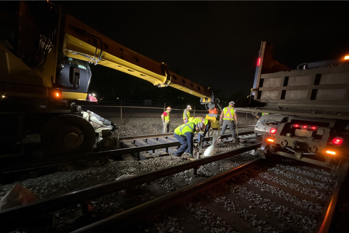 five crew members in reflective vests and hard hats working on tracks at night under floodlights