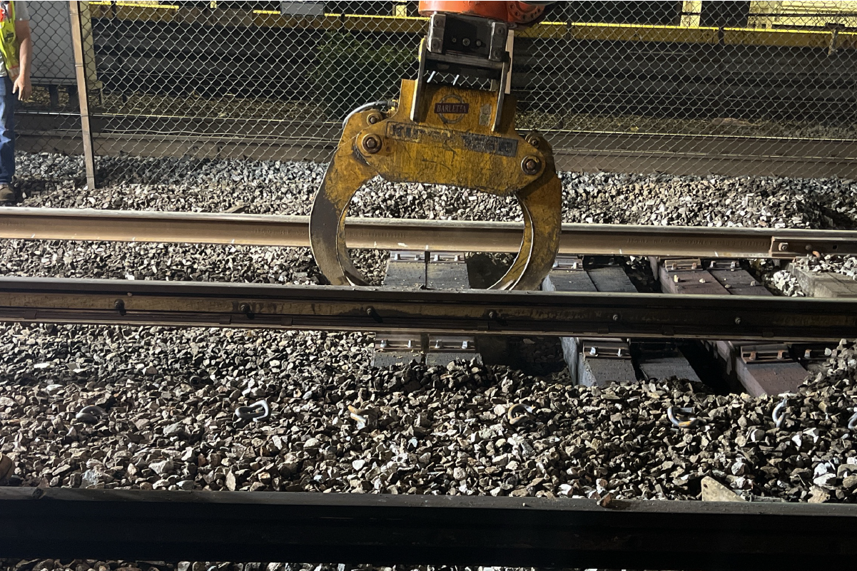 a close up of claw-like equipment grabbing track ties under floodlights at night