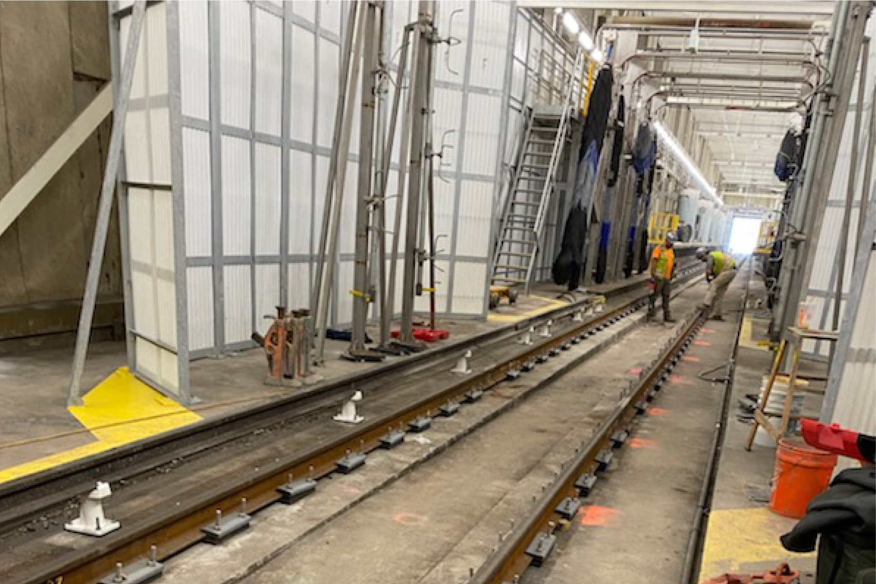 two crew members working near tracks inside a warehouse type building