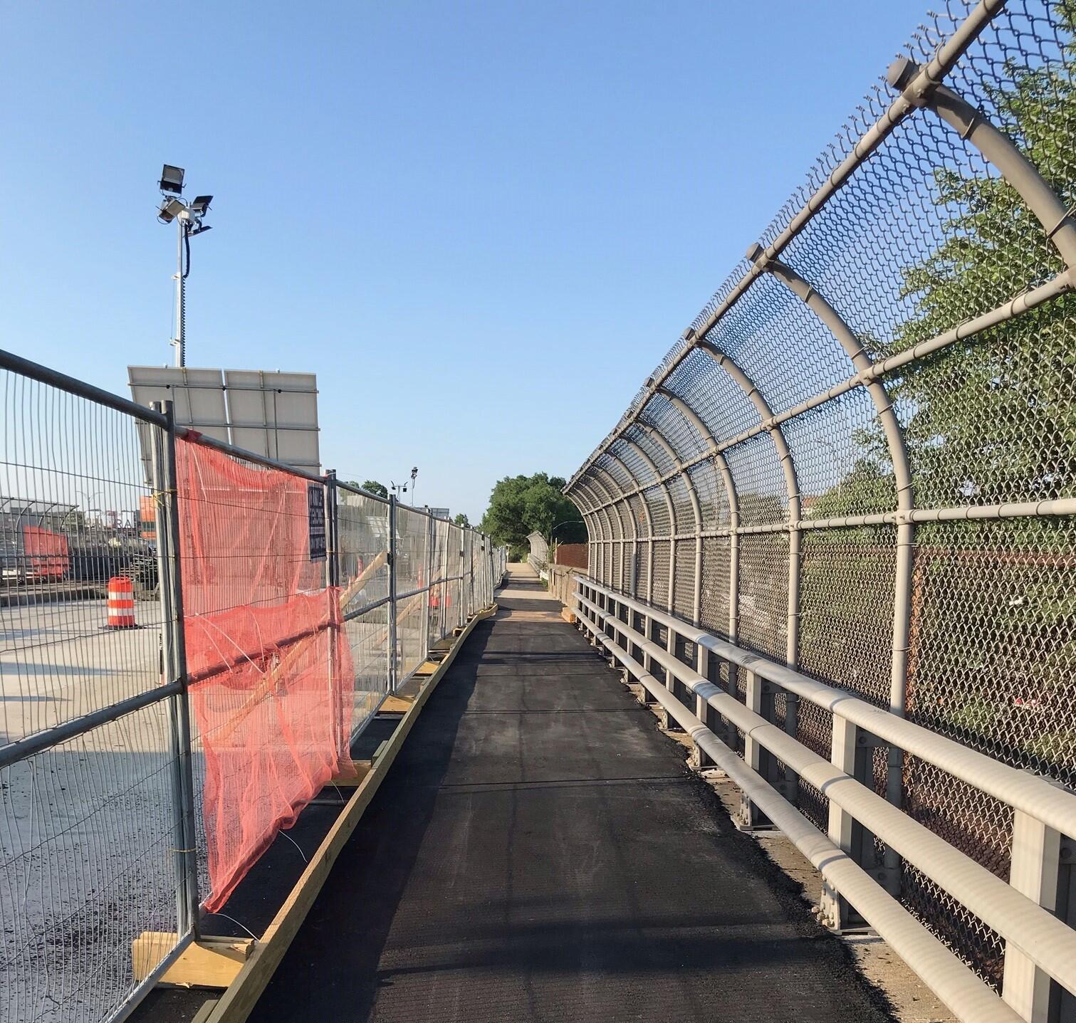 view of pedestrian walkway over a bridge with tall fencing 
