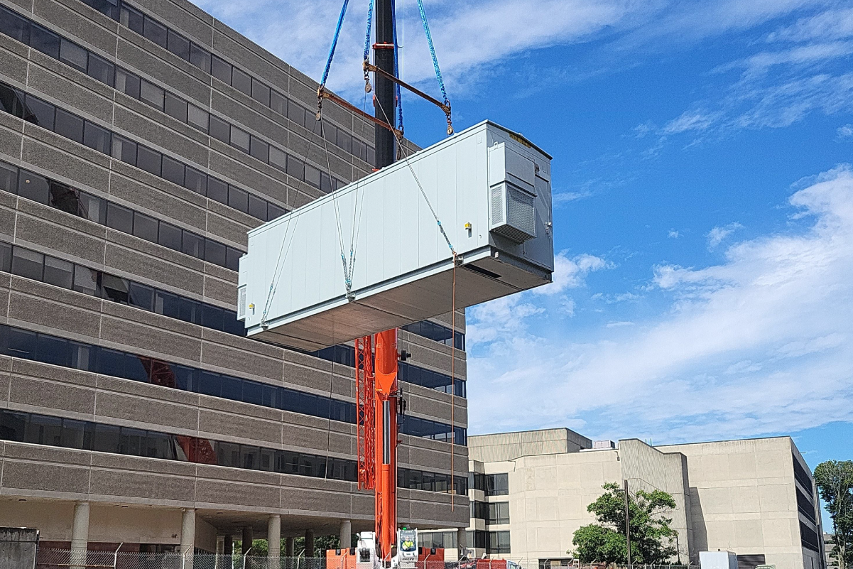 a small portable type building up in the air being lifted by crane