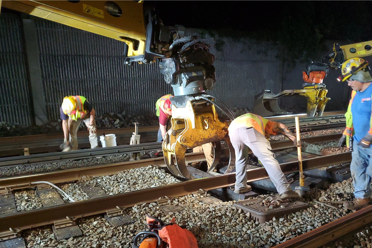 five crew members in reflective vests and hard hats working on tracks in a tunnel