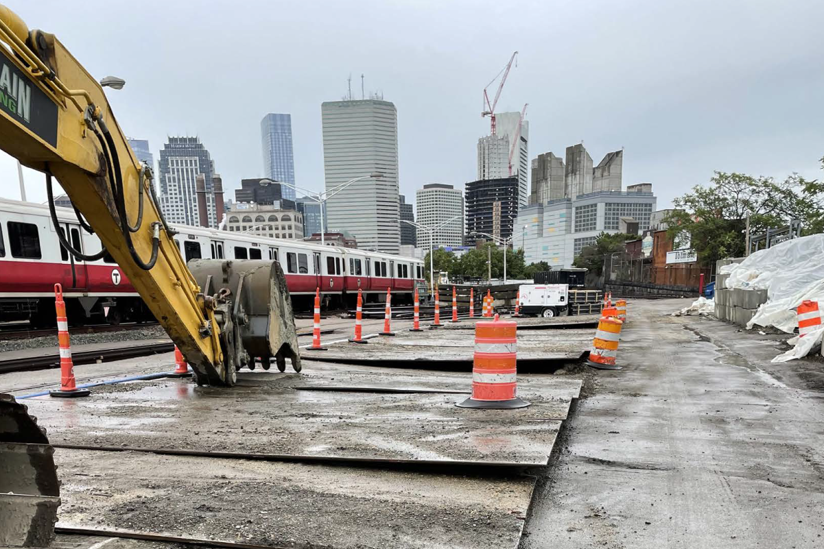 construction equipment with red line train and boston skyline in background