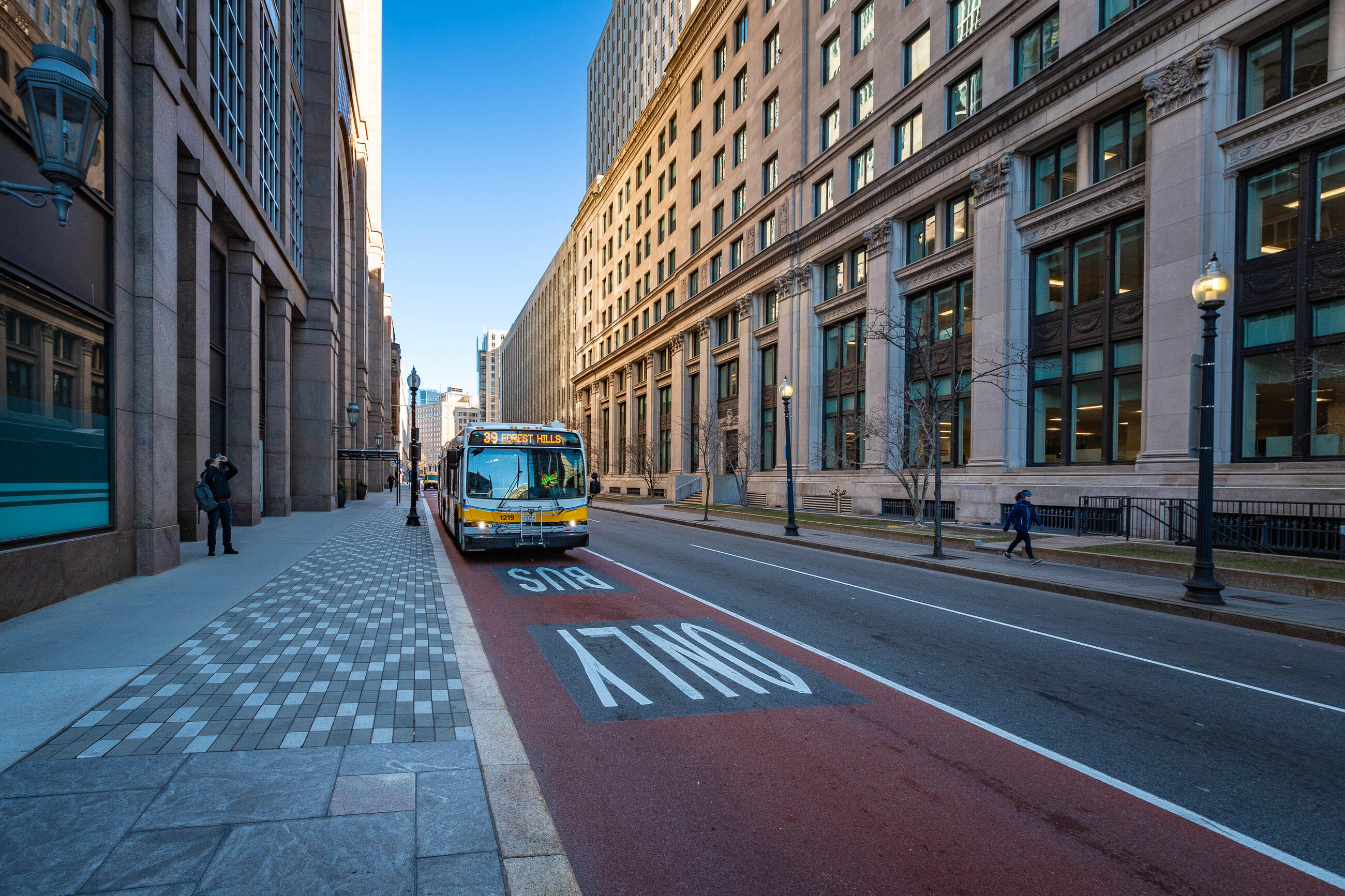 Bus driving down clear path in the designated bus lane, between two tall buildings