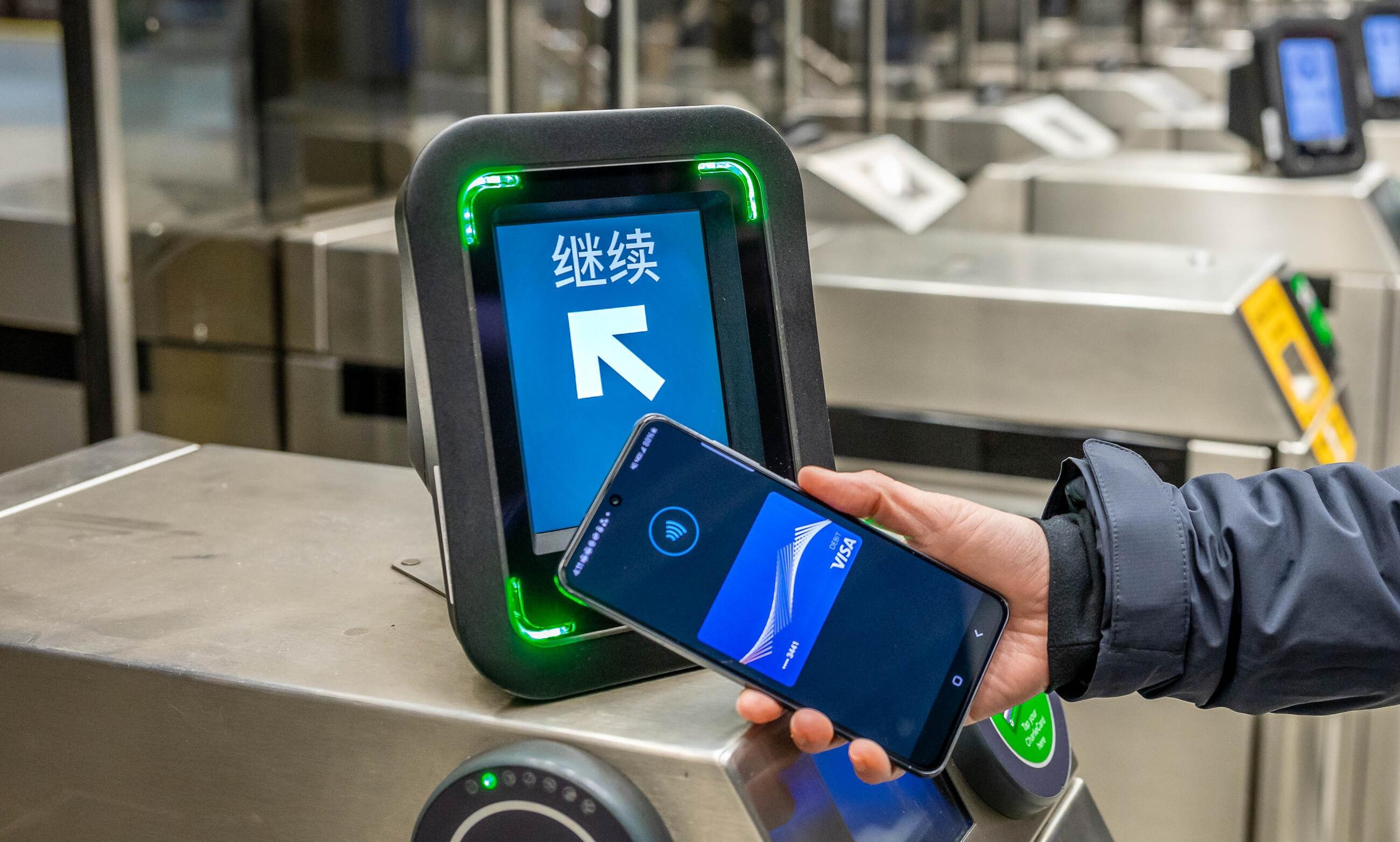 Rider tapping their mobile wallet at a fare gate reader with Go in Simplified Chinese and an arrow on a green screen