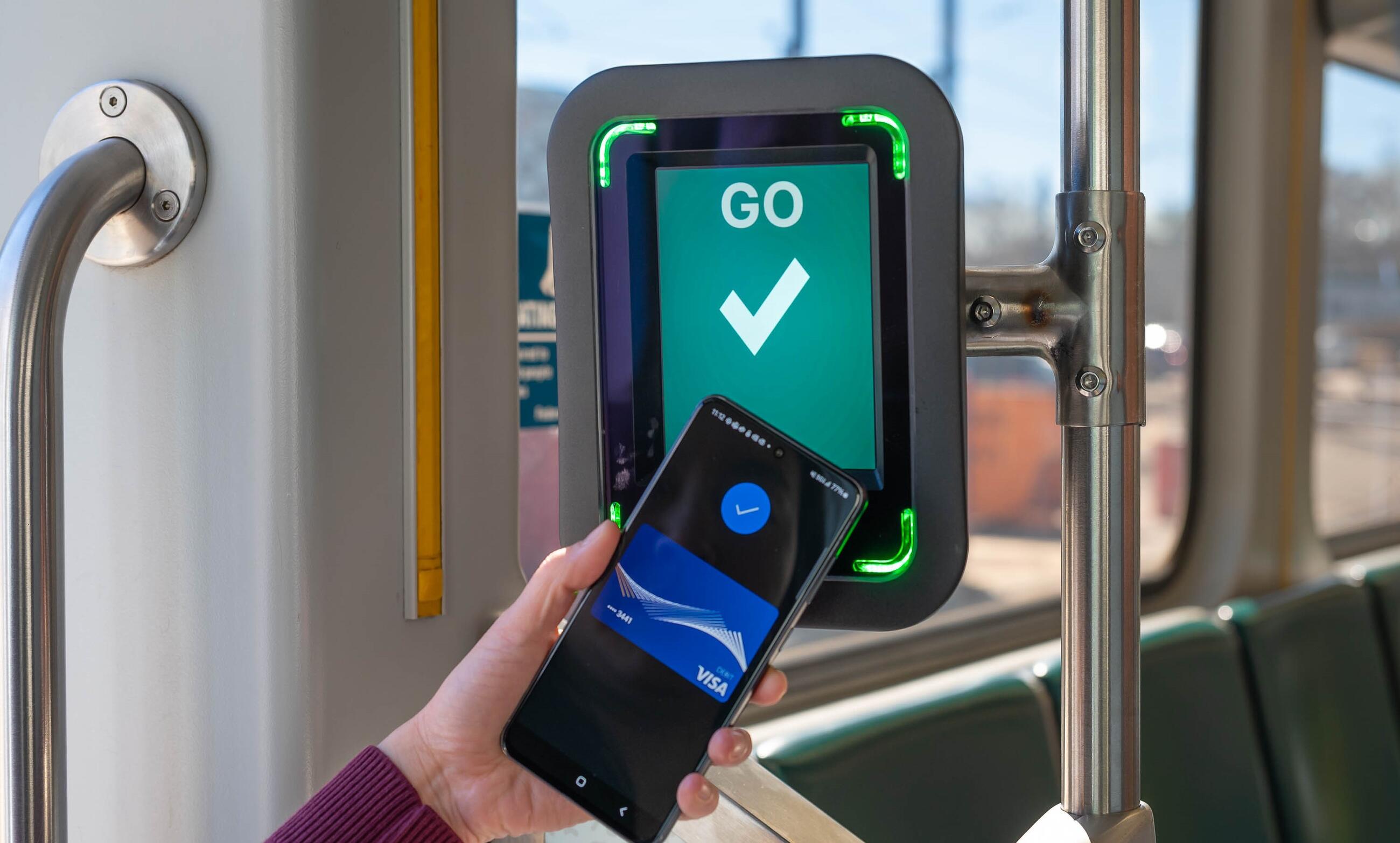 Rider tapping phone on Green Line reader that reads go at the door of a Green Line vehicle