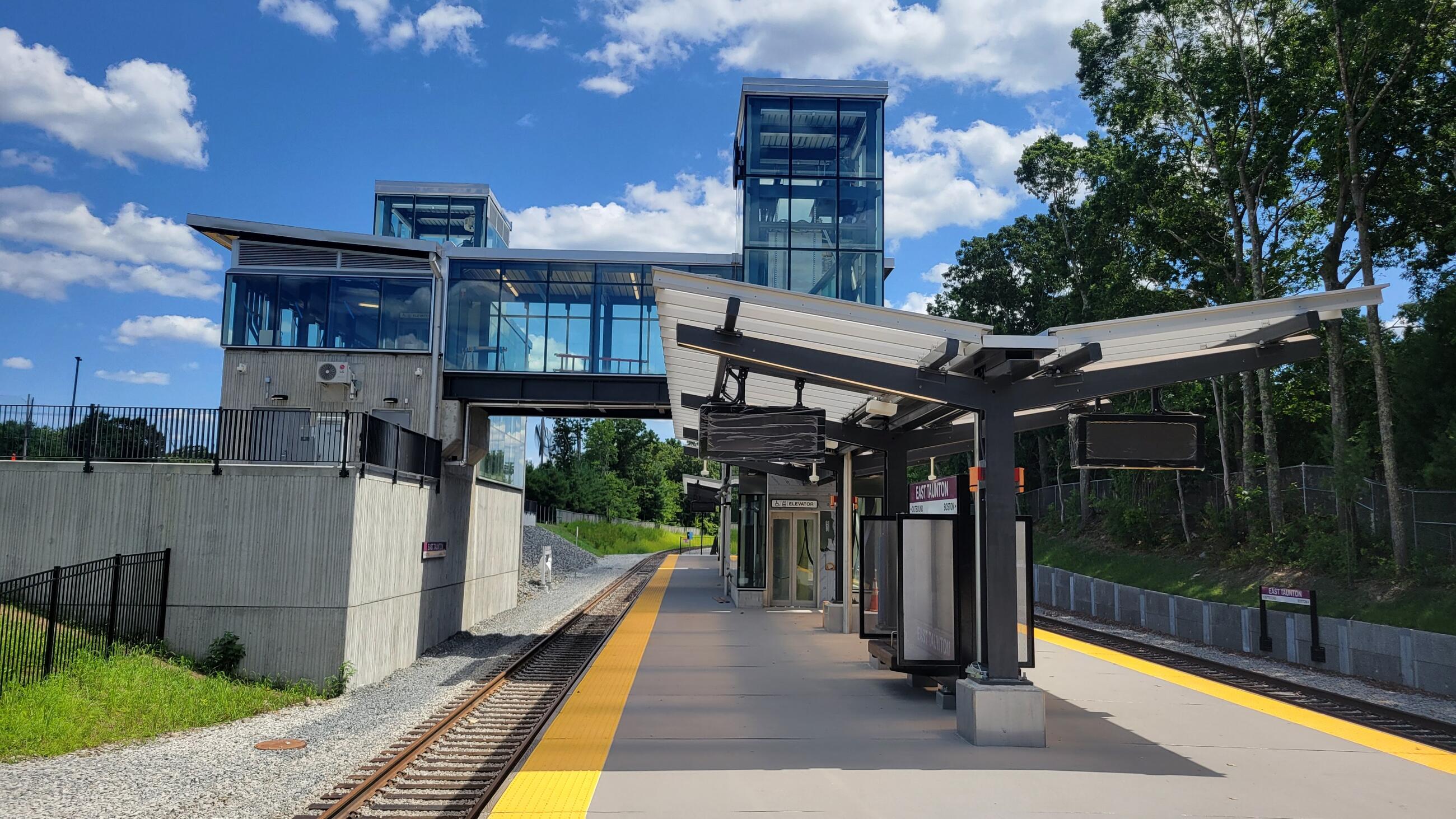 Train platform with an enclosed elevated pedestrian bridge leading to it.