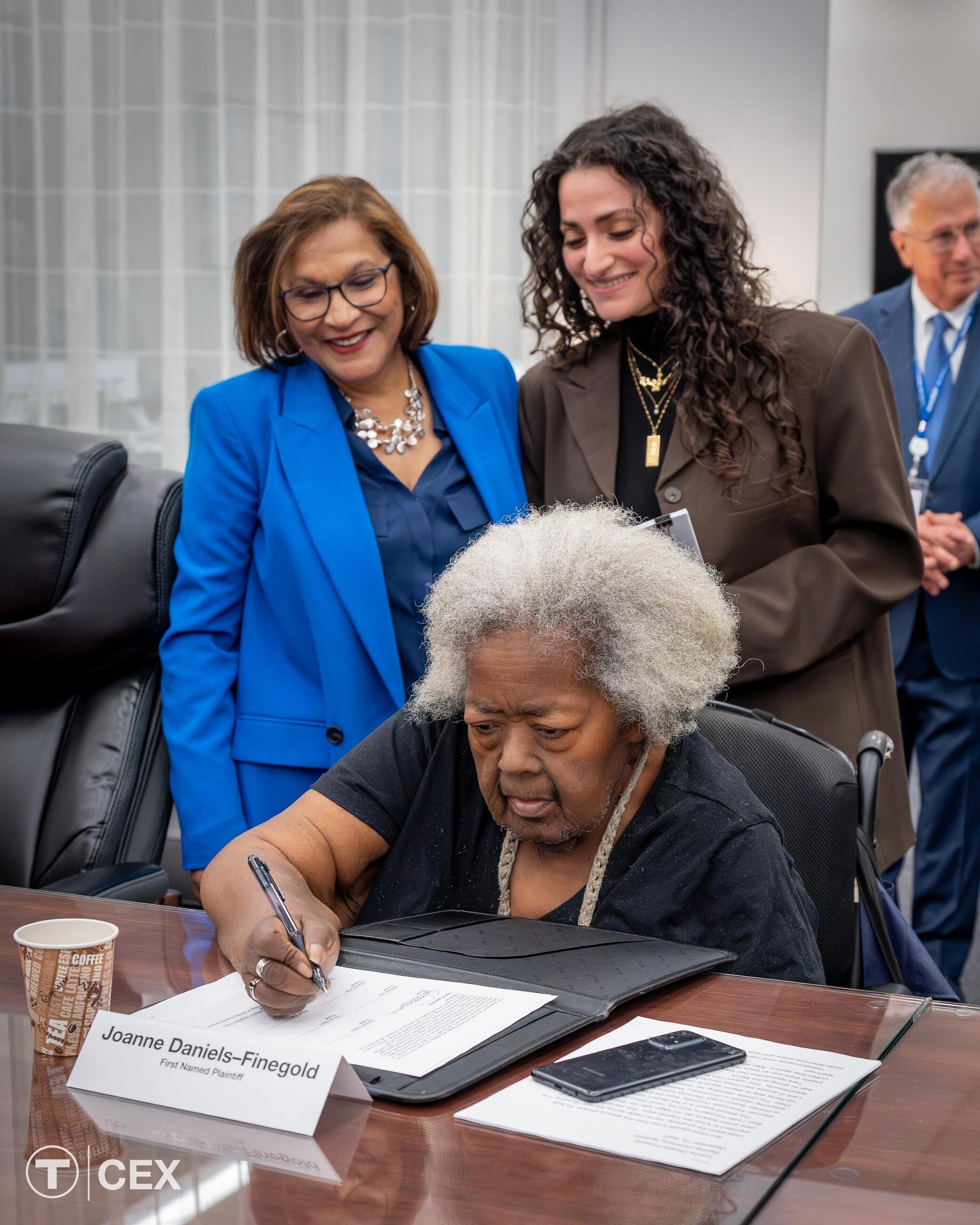 First-named Plaintiff Joanne Daniels-Finegold signing the agreement.