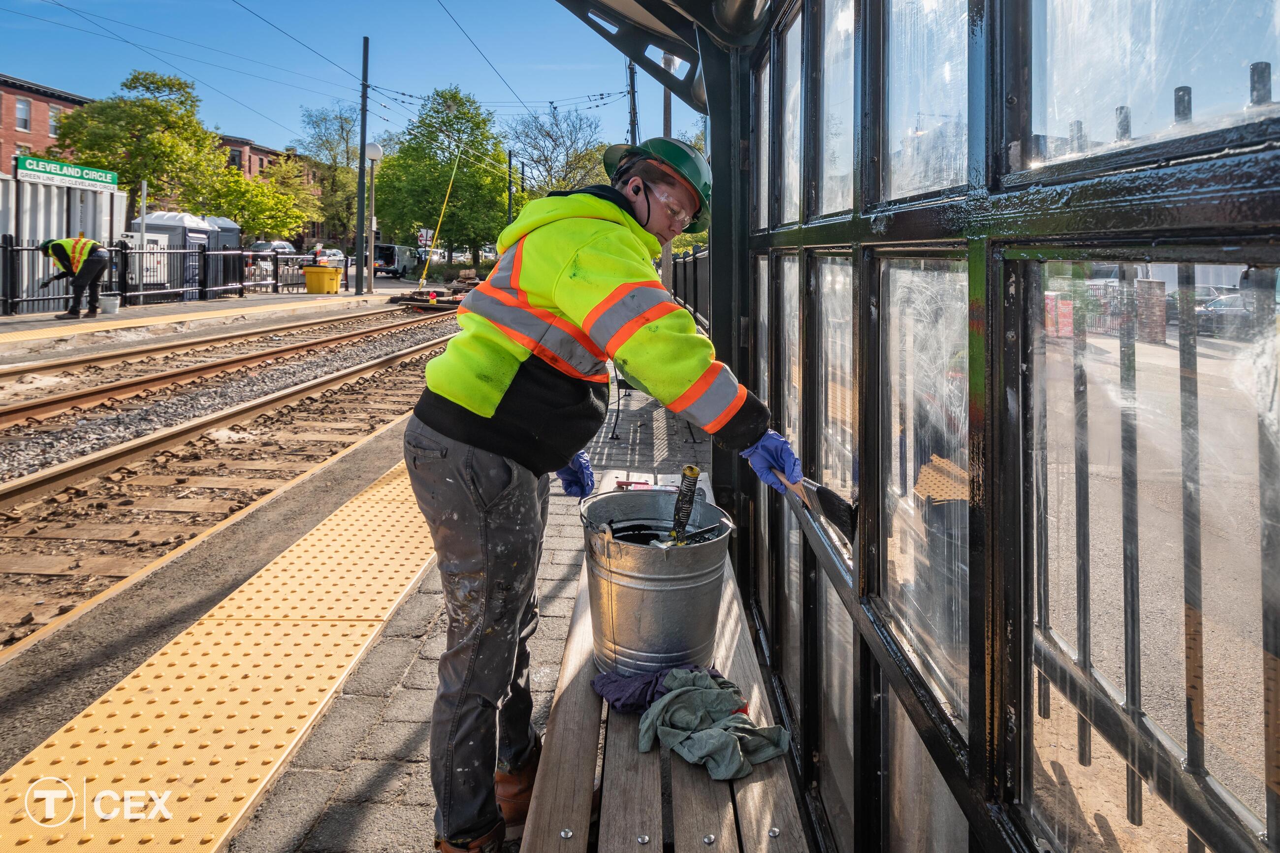 Person paints black along the edge of a divider at a ground level station