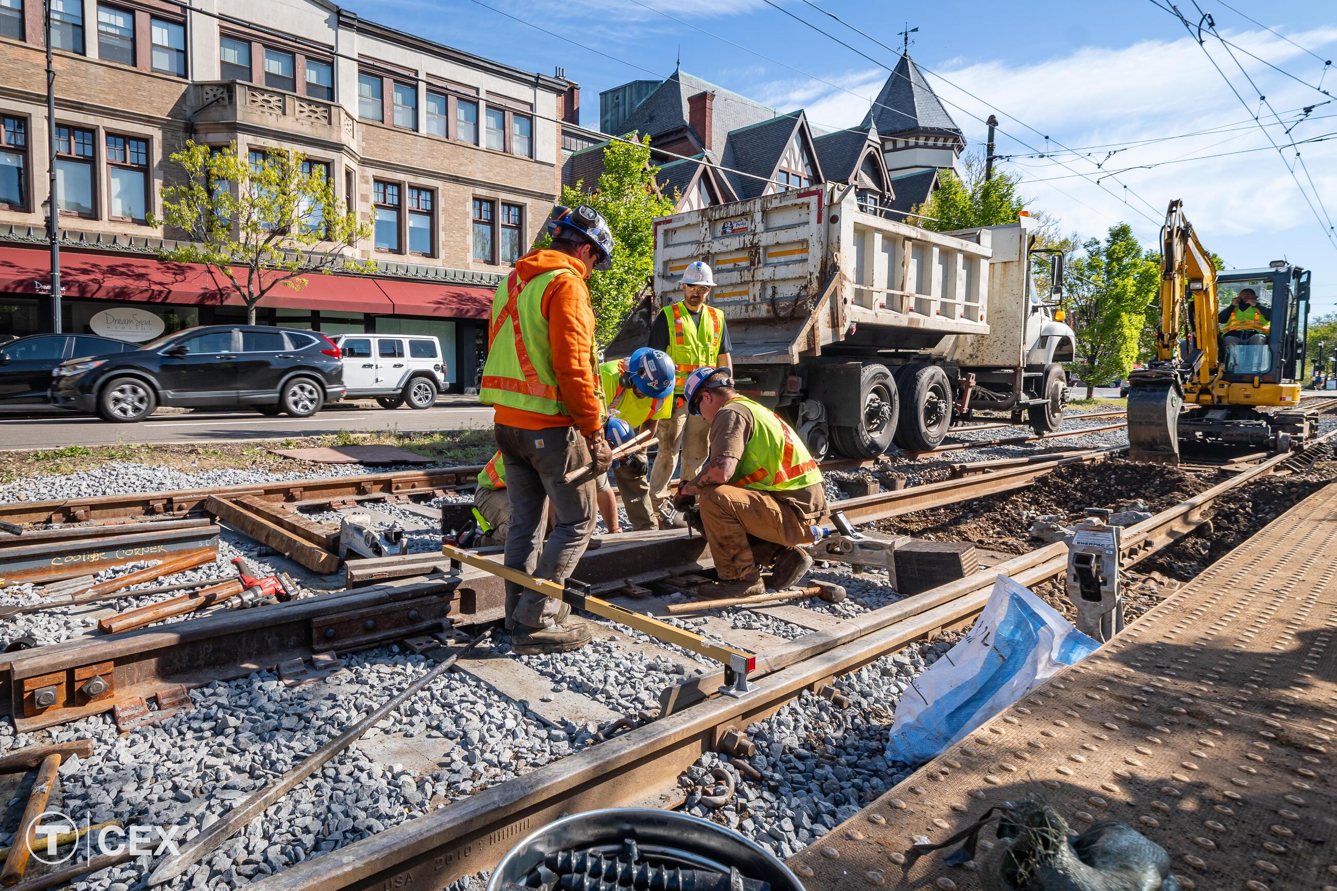Work crews perform maintenance on a rail with buildings behind them