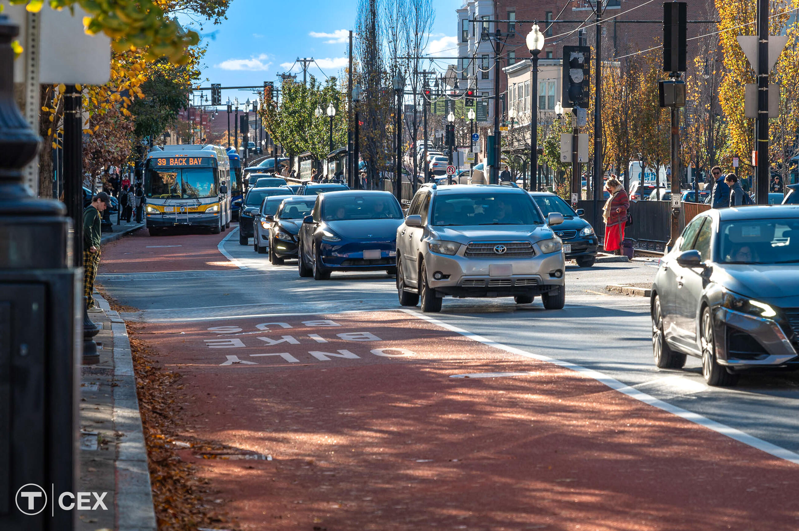 A bus in in the left red-painted bus lane. Cars flow to the right side of it