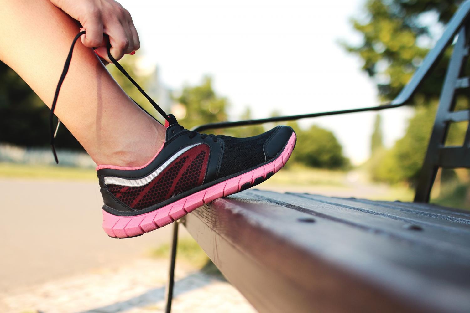 A woman ties her running shoe on a park bench.