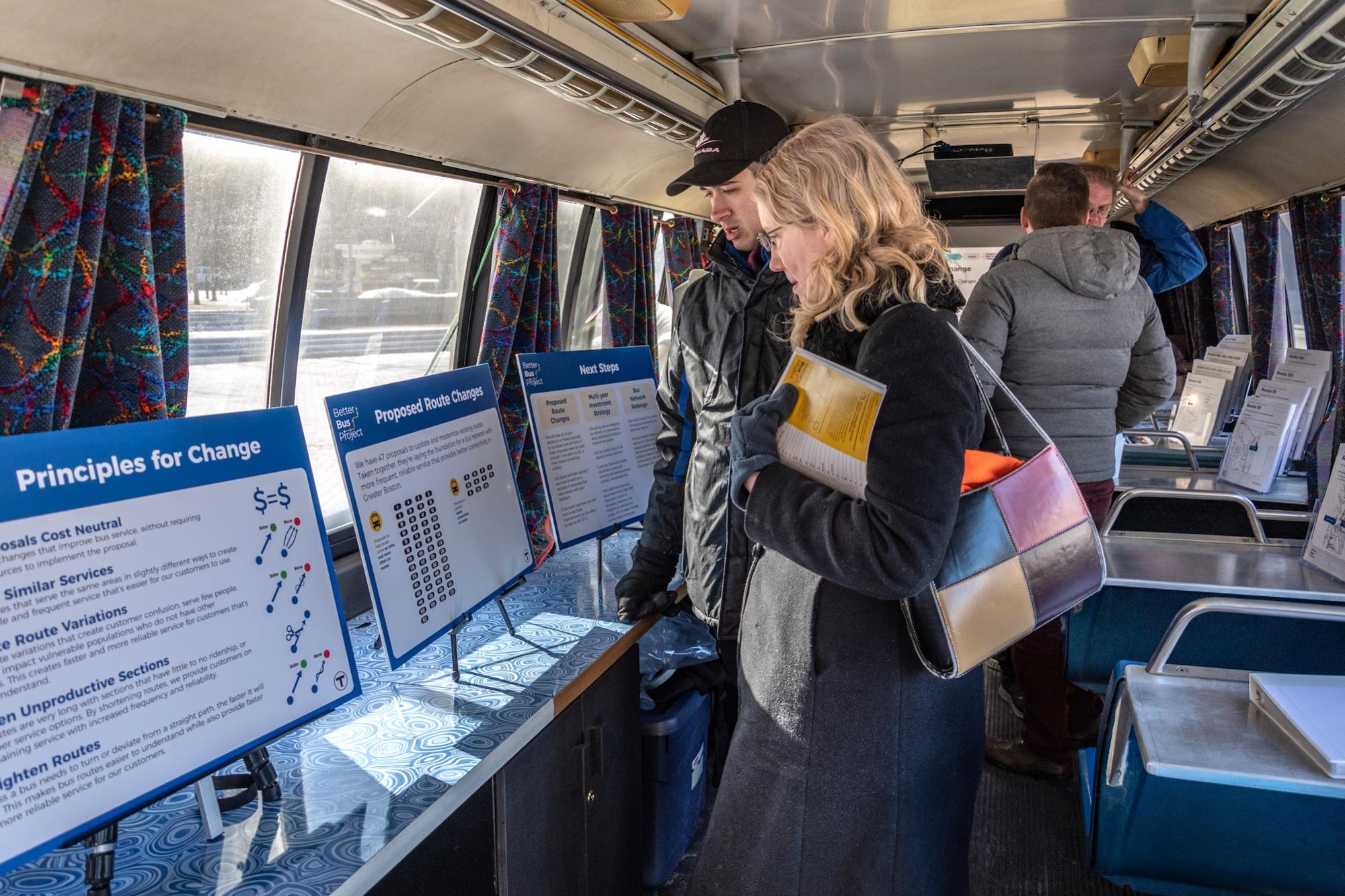Members of the public browse inside a retrofitted bus with tables featuring informational posters and flyers about the Better Bus Project.