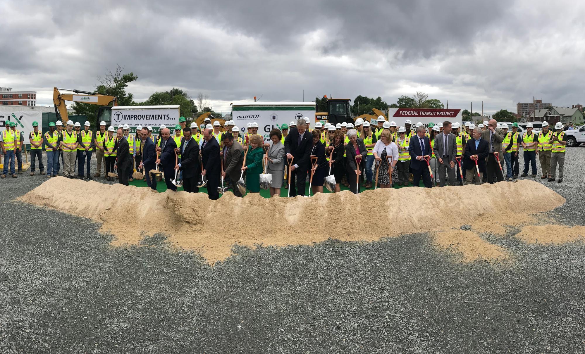 State officials pose with shovels at the Green Line Extension's groundbreaking ceremeony, with construction workings lined up as well