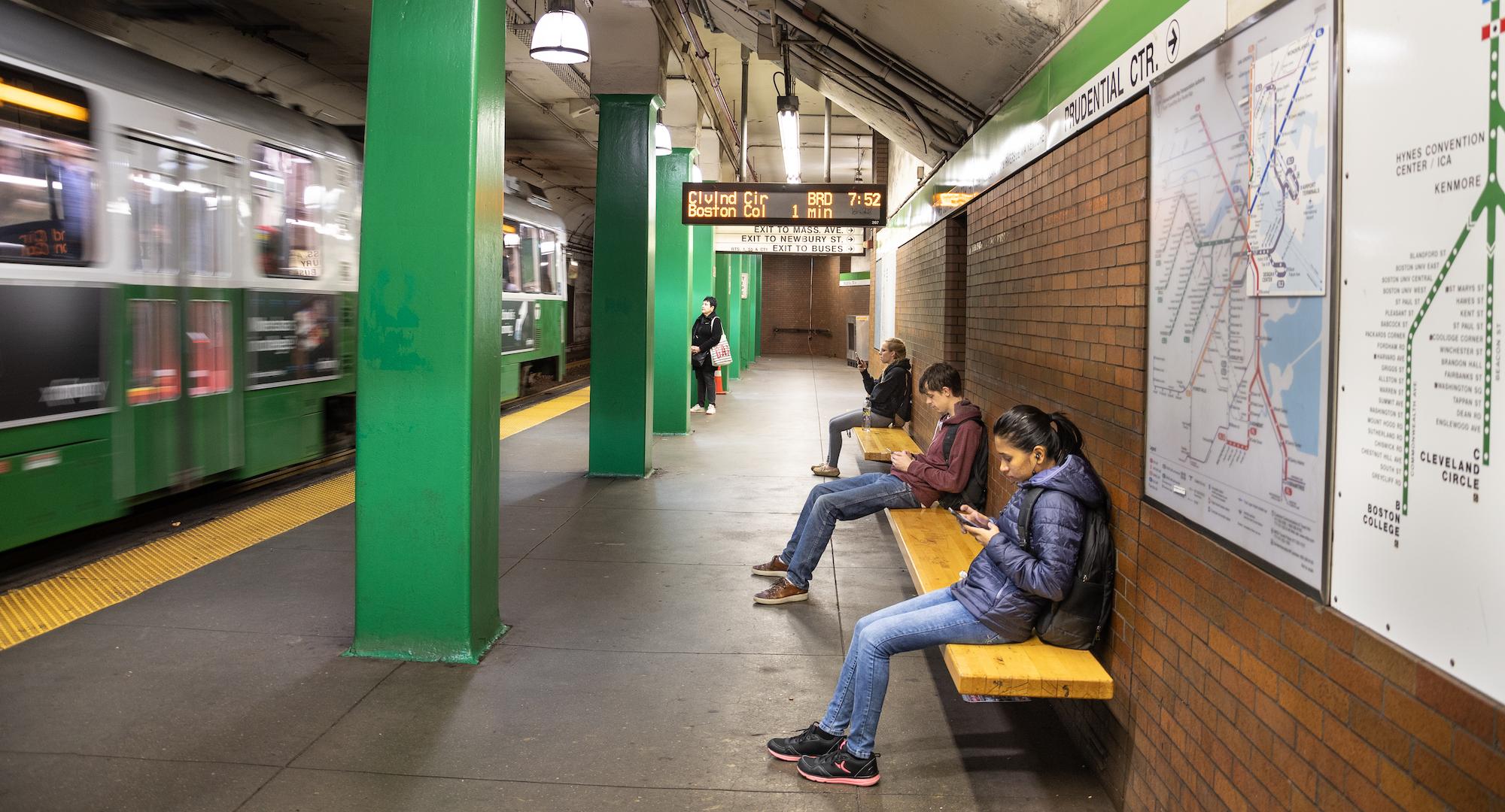 Riders wait for the Green Line at Hynes, checking their smartphones