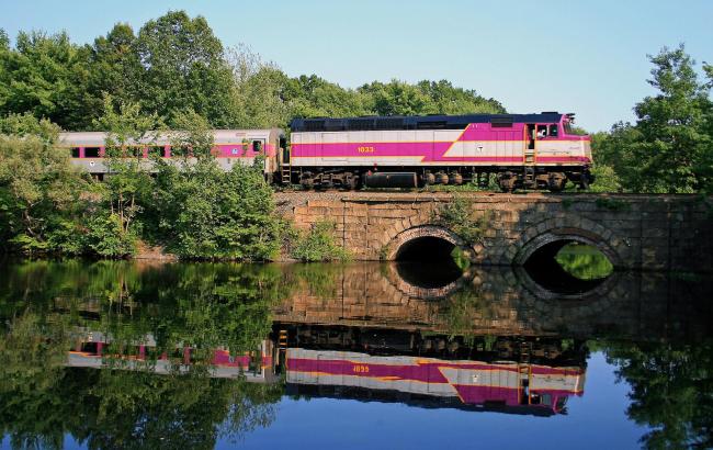 Commuter Rail train crossing a bridge over a river, with lush greenery