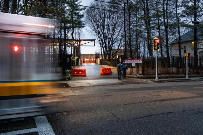 View of Quincy Adams gate from the street, with a bus whirring past, coming from the left