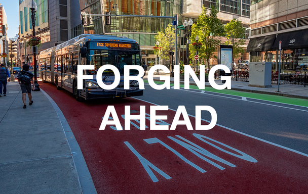 Bus in a bus lane, with "Face coverings required" in its headsign. Overlaid text reads "Forging Ahead."