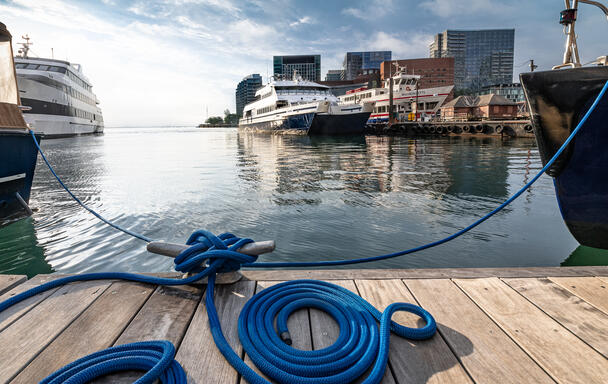 A photo of a ferry in the water, taken from the Rowes Wharf dock. There's a large blue rope tied to the dock in the foreground.
