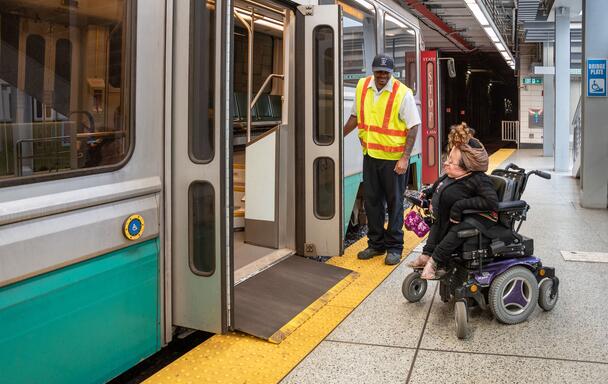 On the Green Line, an operator stands by the doors, as the bridge plate allows a rider in a wheeled mobility device to board