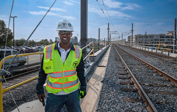 A GLX inspector in a hard hat and high vis vests smiles next to new train tracks