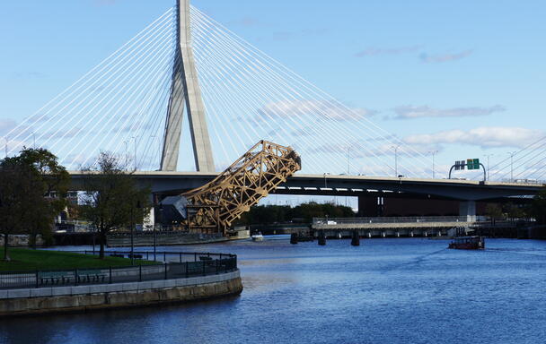 a bridge near north station is partially raised over water. the zakim bridge is in the background