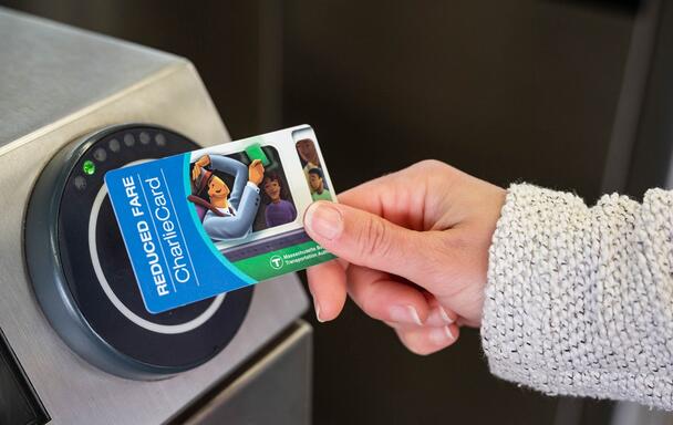 Rider holding a reduced fare CharlieCard to a fare gate reader